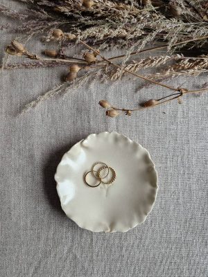 Coupelle au motif végétal contenant des bijoux et posées à côté de fleurs séchées