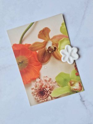 Magnet en grès émaillé blanc en forme de fleur posé sur une carte postale