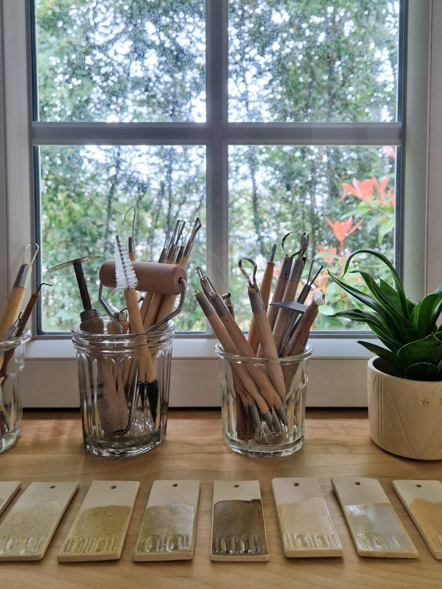 Outils de poterie et plante verte posés devant une fenêtre donnant sur la nature