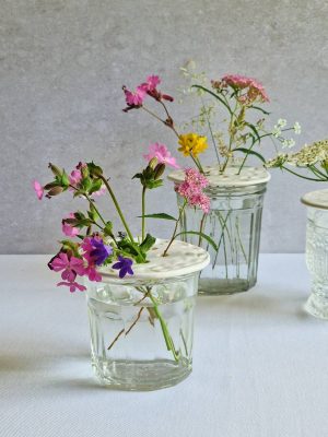 Plusieurs compositions de bouquets avec pique-fleurs en céramique posés sur des contenants en verre