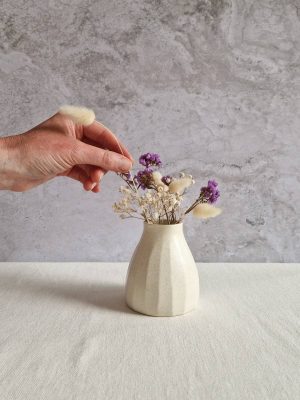 Main disposant des fleurs séchées dans le vase Astrée