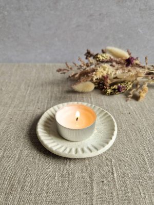 Mini coupelle contenant une bougie chauffe-plat allumée avec des fleurs séchées en arrière-plan