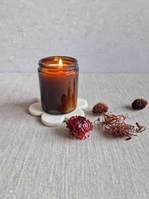 Support Marguerite avec une bougie allumée dans un contenant en verre ambré et quelques fleurs séchées éparpillées autour