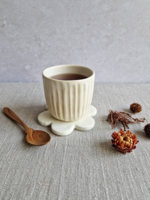 Support Marguerite utilisé en dessous de verre pour un gobelet de thé, posé à côté d'une cuillère en bois et de quelques fleurs séchées